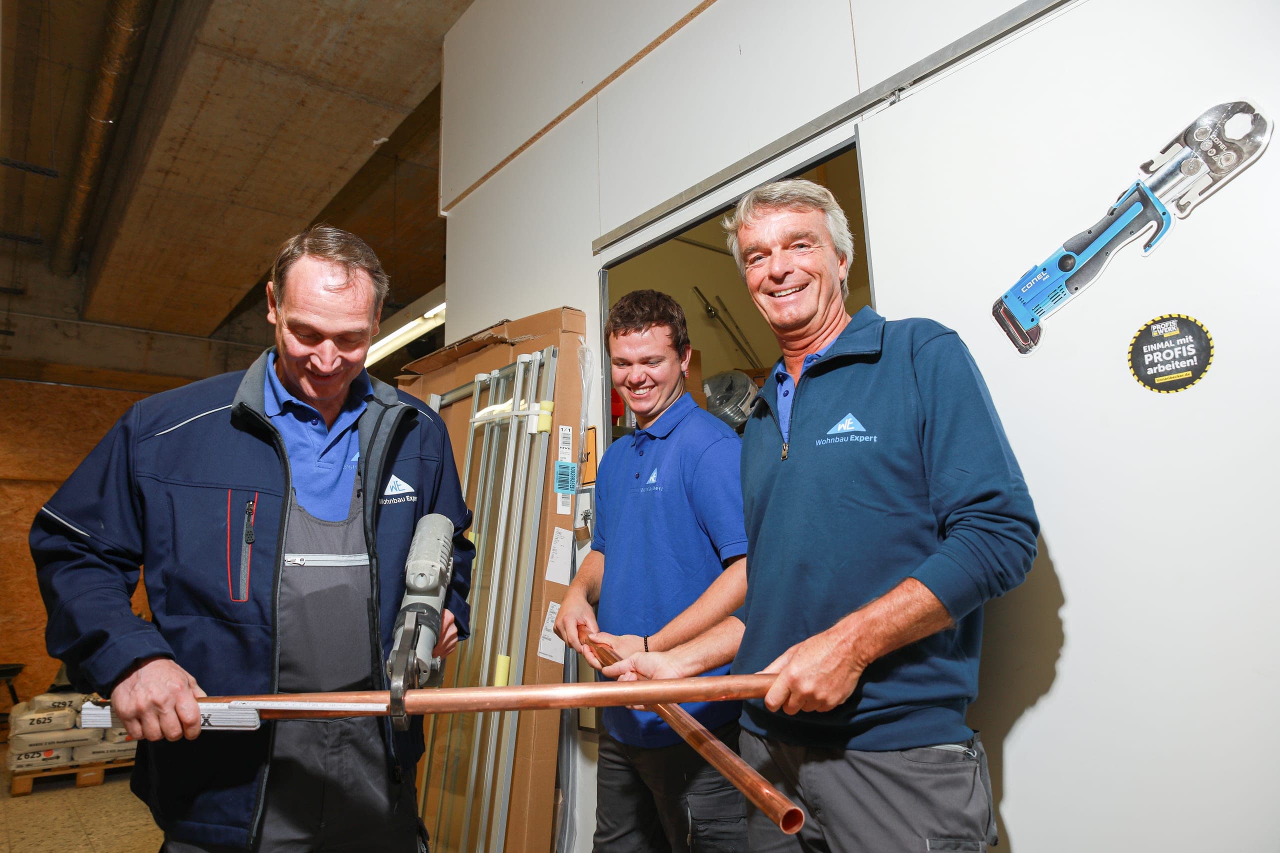 Drei Handwerker von Wohnbau Expert in der Werkstatt mit einem Kupferrohr