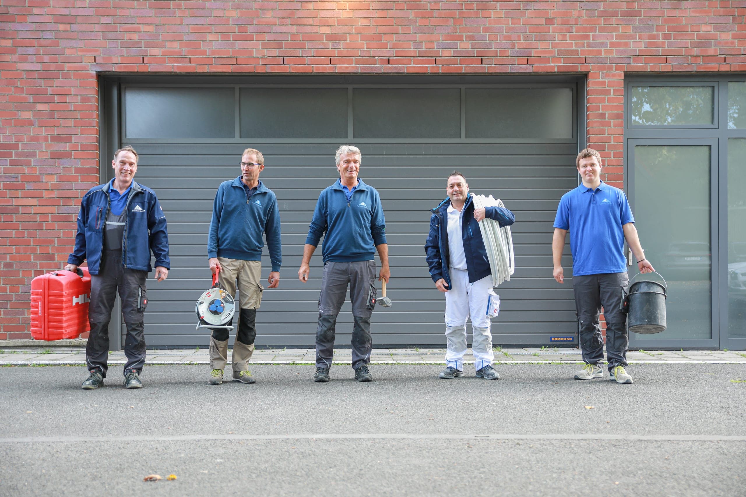 Das Team von Wohnbau Expert mit Werkzeug vor dem Betriebsgebäude in Münster